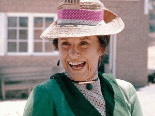 an elderly woman wearing a straw hat and a green jacket is smiling .