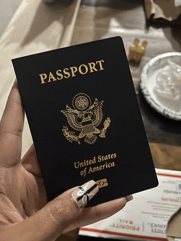 a black passport from the united states of america is held in a woman 's hand