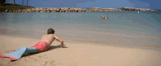 a man in a mermaid tail laying on the beach