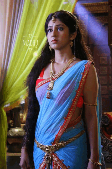 a woman in a blue and red saree with the word madhu on the bottom right