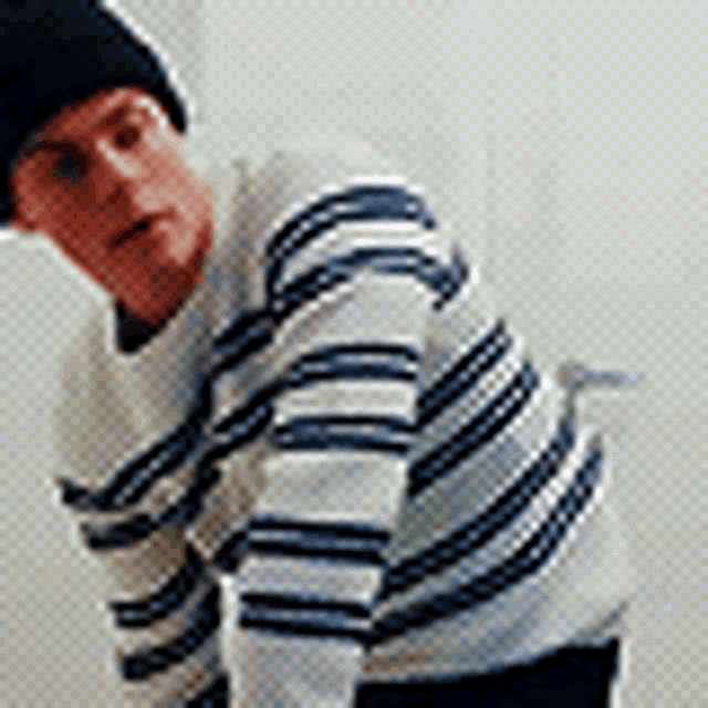 a man wearing a black hat and a striped sweater is standing in front of a white wall .