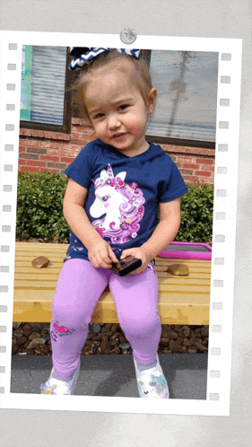 a little girl is sitting on a bench wearing a unicorn shirt