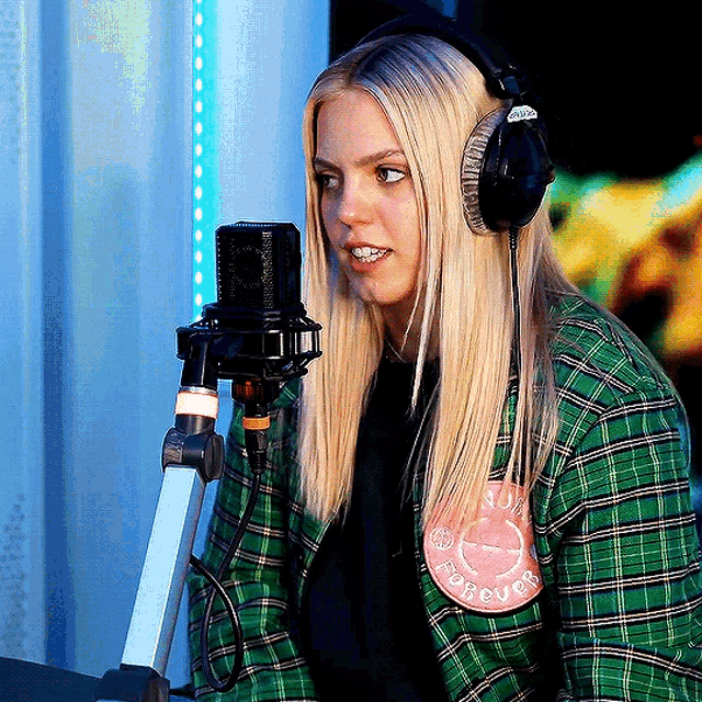 a woman wearing headphones stands in front of a microphone with a forever patch on her shirt