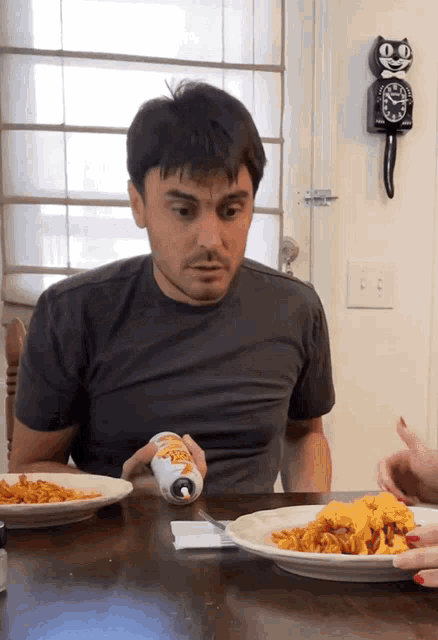 a man sitting at a table with a plate of food and a clock on the wall that says ' ee '