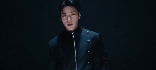 a young man in a black jacket is dancing in front of a blue wall .