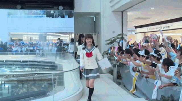 a girl in a school uniform is walking in front of a crowd in front of a sign that says ' women world gallery '