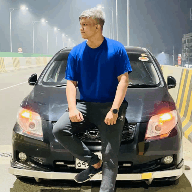 a man in a blue shirt leans on a black car