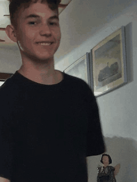 a young man in a black shirt smiles in front of a wall with a picture on it