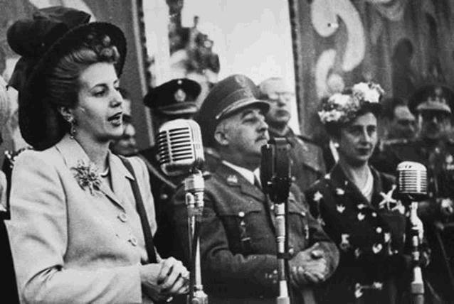 a woman is singing into a microphone while standing in front of a crowd of people in military uniforms .