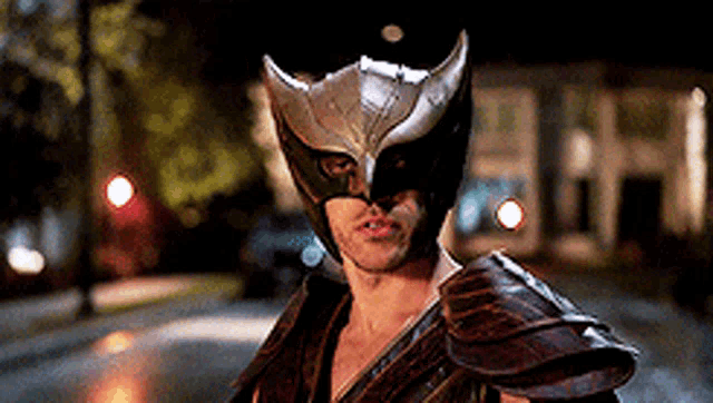 a man wearing a owl mask and armor stands on a street at night