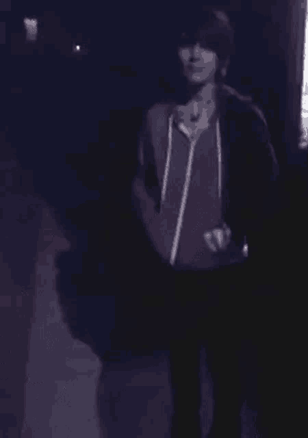 a man in a red hoodie is walking down a dark street at night .