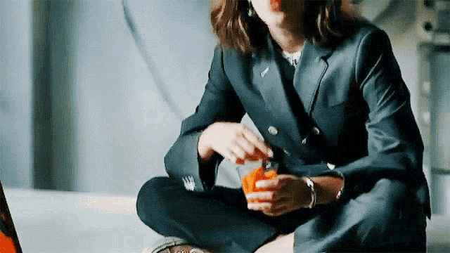 a woman in a suit is sitting on the floor with her legs crossed and eating a piece of food .