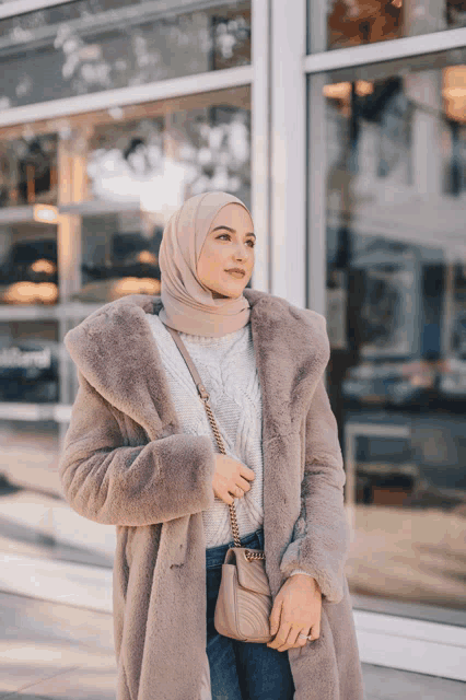 a woman wearing a hijab and a fur coat stands in front of a store