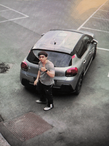 a man is standing in front of a silver car that says citroen on the back