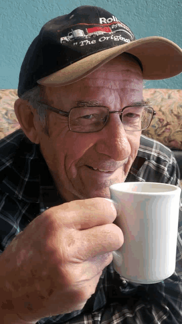 a man wearing a hat that says " the original " is drinking from a cup