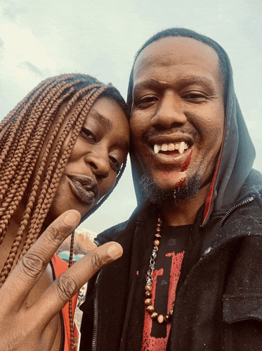 a man with vampire teeth and a woman with braids posing for a photo