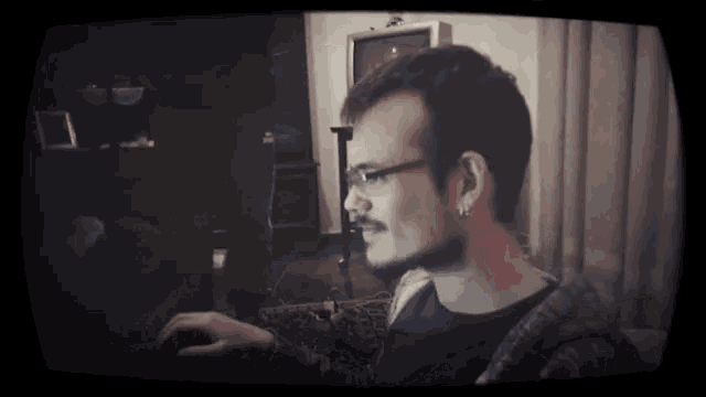 a man with a beard and ear piercings is sitting in front of a tv