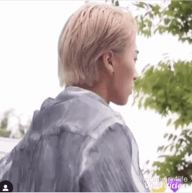 a man with blonde hair is standing in front of a tree wearing a clear jacket .