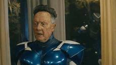 a man in a blue superhero suit is standing in front of a window .