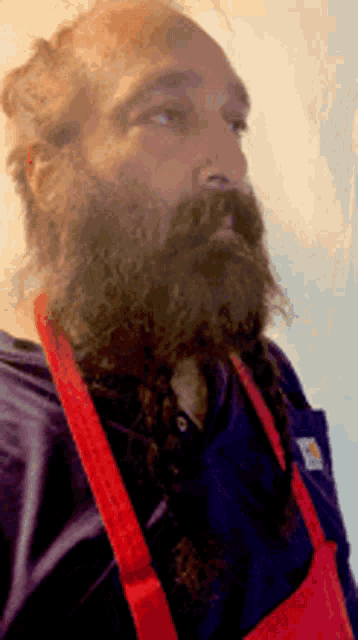 a man with a beard wearing a red apron and a carhartt shirt
