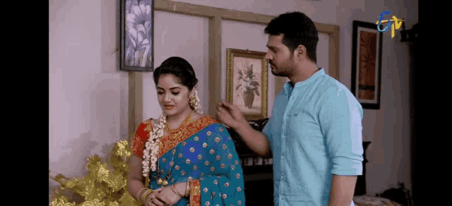 a man and a woman are standing next to each other in a living room . the woman is wearing a blue saree .