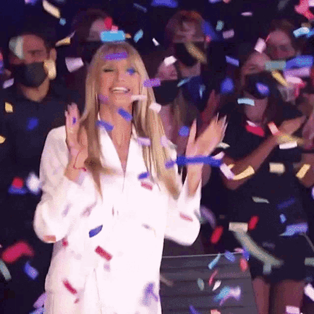 a woman in a white shirt stands in front of a crowd of people while confetti is falling around her