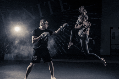 a woman in boxing gloves is kicking a man in front of a sign that says ignite