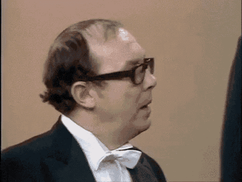 a man in a tuxedo and bow tie is making a surprised face .