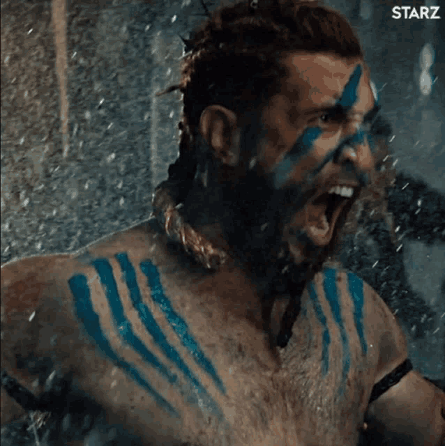 a man with blue paint on his face and chest is screaming