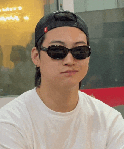 a young man wearing sunglasses and a hat with a red t on it