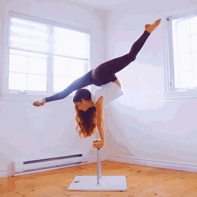 a woman doing a handstand on a pole in front of a window
