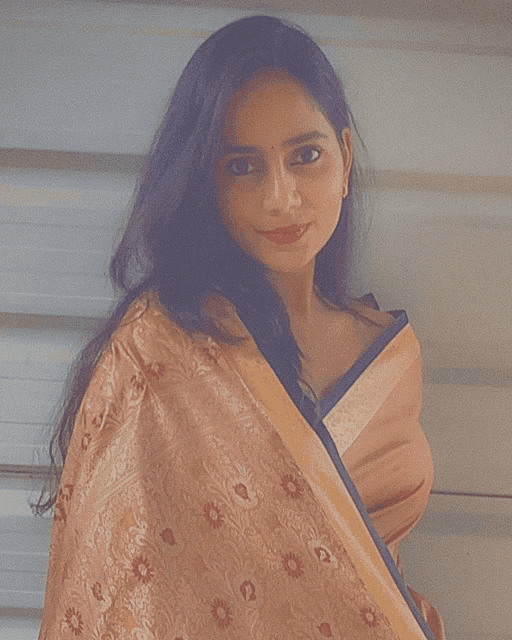 a woman wearing a peach and gold colored embroidered shawl stands in front of a white wall