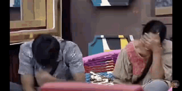 a man and a woman are sitting next to each other on a couch covering their faces .