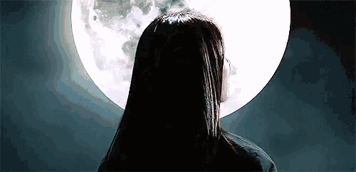 a woman is standing in front of a full moon in a dark room .
