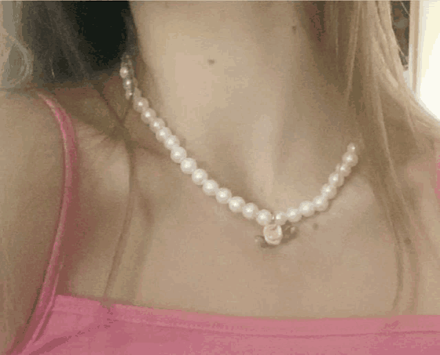 a woman is wearing a pearl necklace with a pink rose pendant