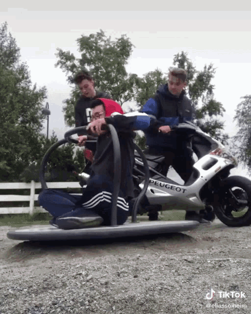 a group of young men are riding a peugeot scooter on a gravel road