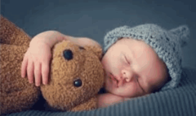 a newborn baby is sleeping with a teddy bear .