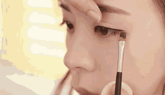a woman is applying eye shadow with a brush to her eye .