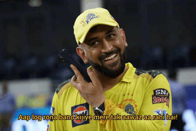 a man wearing a yellow super kings hat is smiling and holding a cell phone