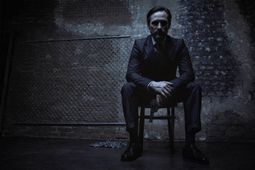 a man in a suit and tie is sitting on a chair with his hands folded