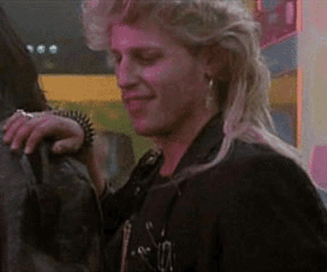 a woman wearing a mullet and a black jacket is standing next to a man .
