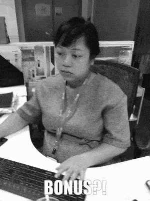 a woman is sitting at a desk typing on a keyboard with the words bonus written on the keyboard .
