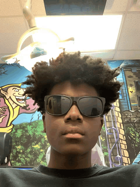 a young man wearing sunglasses in front of a mural of a cartoon character