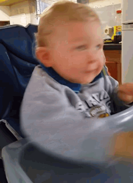 a baby is sitting in a high chair with a bowl of food and a bottle of sprite in the background