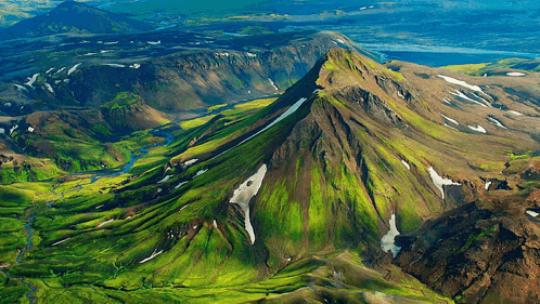 an aerial view of a mountain covered in green grass and snow