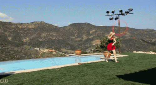 a woman in a red dress is playing with a hula hoop by a pool with mountains in the background