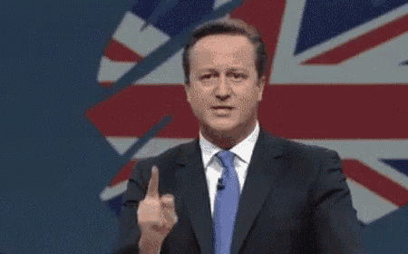 a man in a suit and tie is giving a speech in front of a flag of the united kingdom .