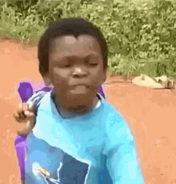 a young boy in a blue shirt is sitting in a chair on a dirt road and making a funny face .