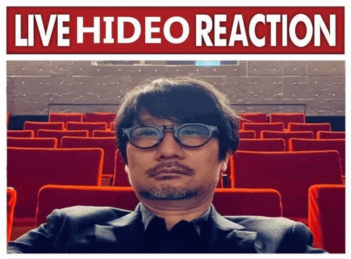 a man in a suit and glasses is sitting in an auditorium with the words live hideo reaction written above him