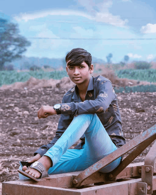 a young man wearing a watch sits on a piece of metal in a field with a rainbow in the background